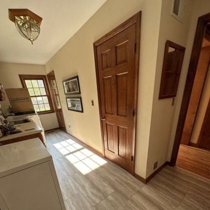 Sunlit hallway with wooden doors, beige walls, and a window casting light on the floor.