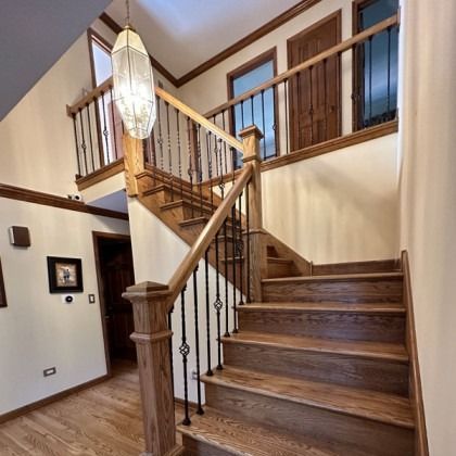 Wooden staircase in a home foyer with railing, chandelier, and upper balcony landing