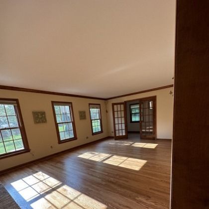 Empty sunlit room with hardwood floors, beige walls, and several windows