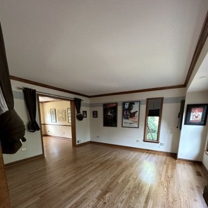 Empty living room with hardwood floors, white walls, dark trim, and framed wall art.