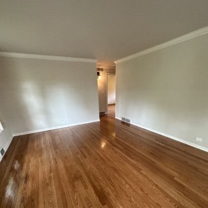 Empty living room with hardwood floors, light walls, and a hallway opening in the center