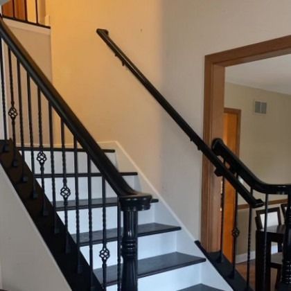 Indoor staircase with black railings and beige walls, viewed from the bottom landing.