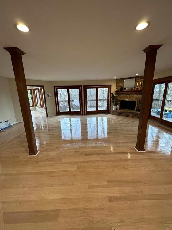 Spacious empty living room with hardwood floors, wood pillars, large windows, and a stone fireplace.