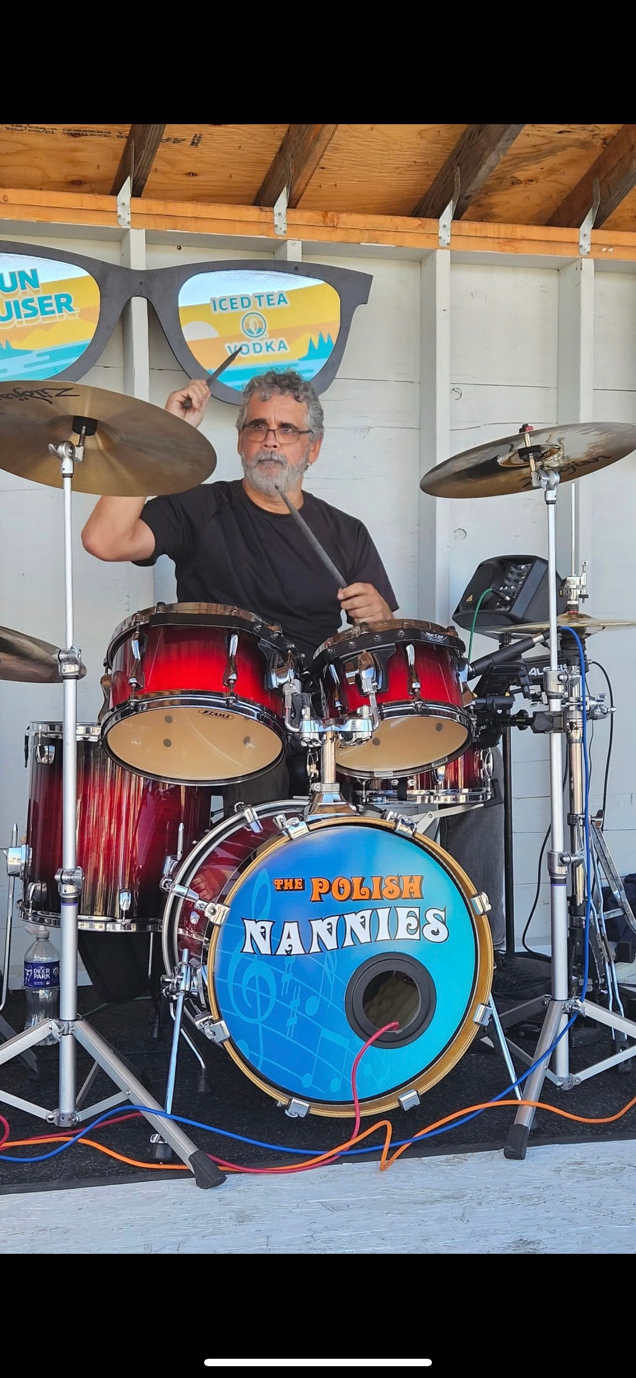 A drummer playing a red drum set. A sign on the front drum reads