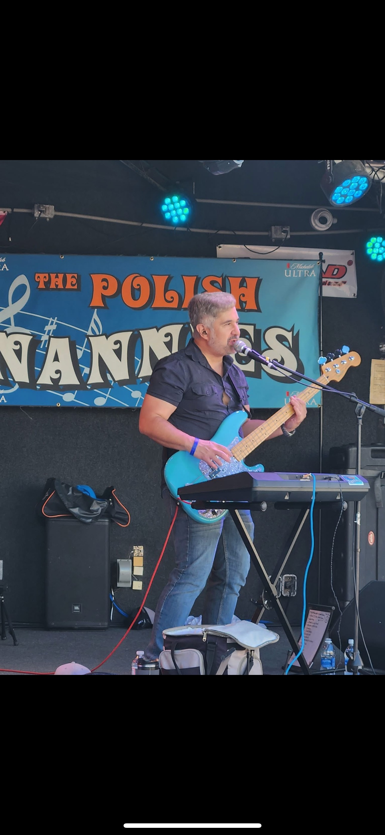 Man playing a blue bass guitar on stage with a band banner that reads