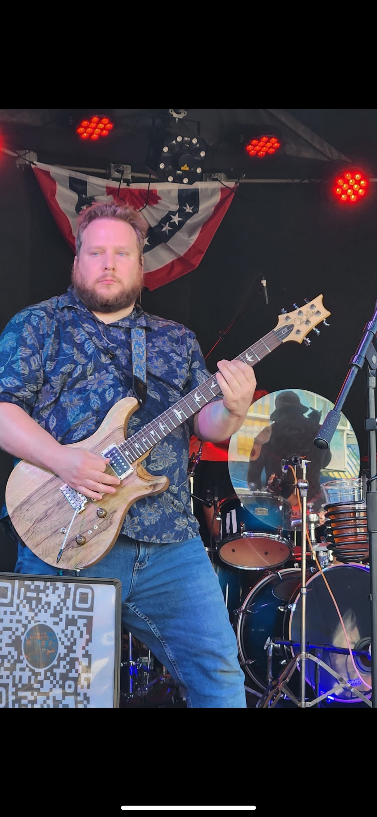A man playing a light-colored electric guitar on stage with a band.