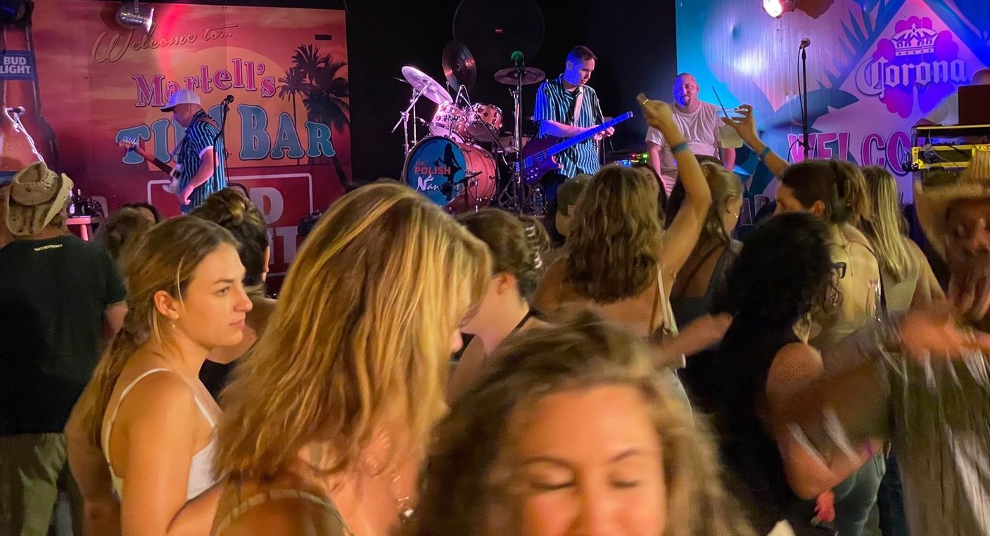 Band performing on stage in a bar, people dancing and enjoying live music.