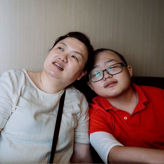 Two people leaning together on a couch; one wears a white shirt, the other a red polo and glasses.
