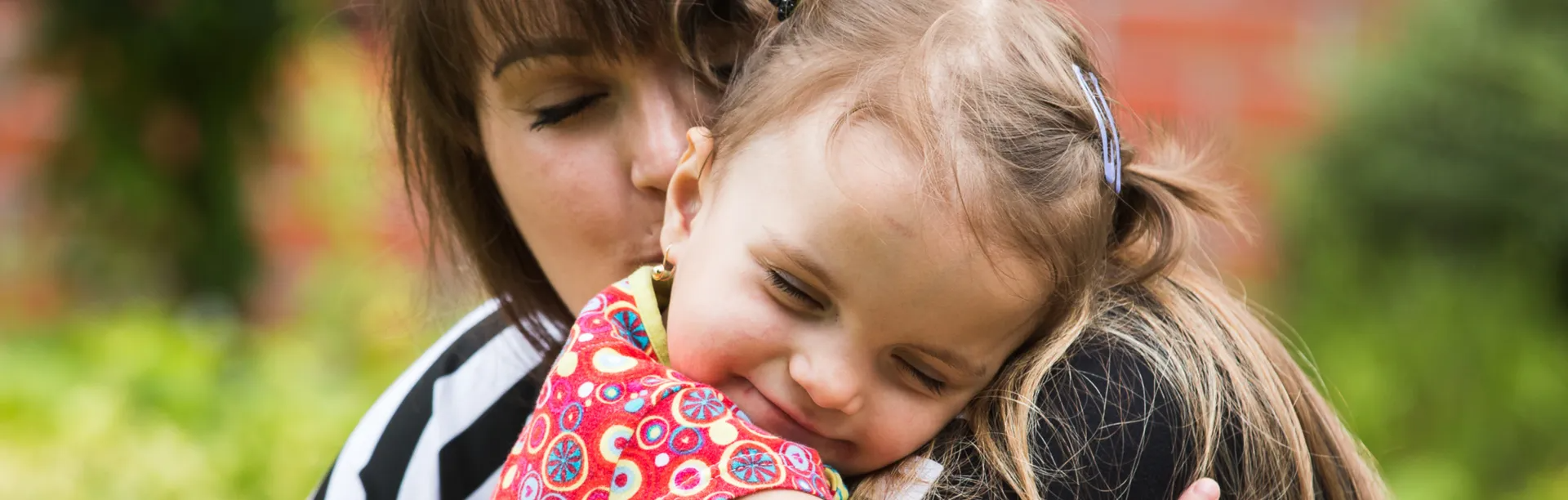 Two people hugging outdoors, one child in a red floral jacket