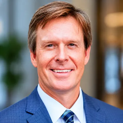 Smiling man in a blue suit and tie against a blurred indoor background