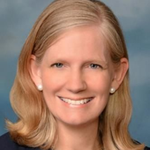Smiling blonde woman in a light shirt against a blue studio backdrop