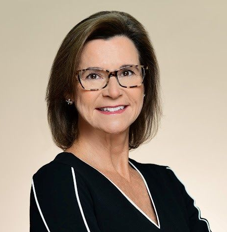 Portrait of a smiling woman wearing glasses and a black blouse against a beige background