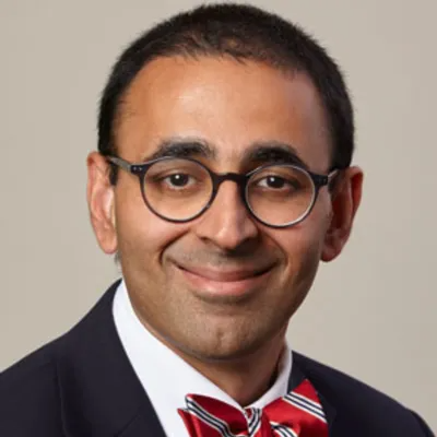Portrait of a man in glasses and a red striped bow tie, smiling against a neutral background