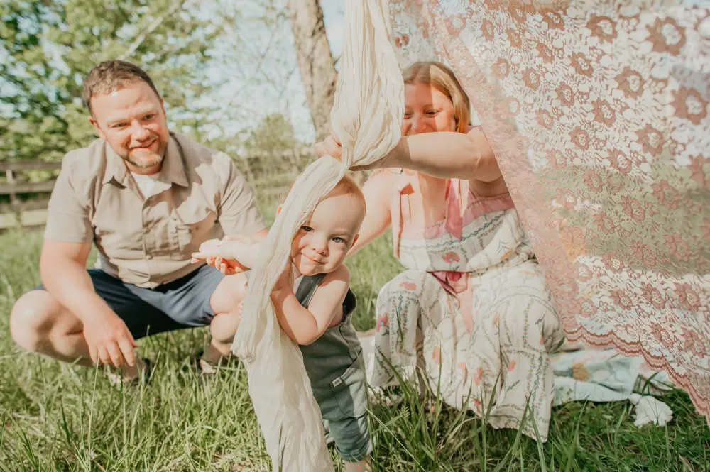 Family sitting in grass beneath a patterned canopy, smiling in a sunny outdoor scene