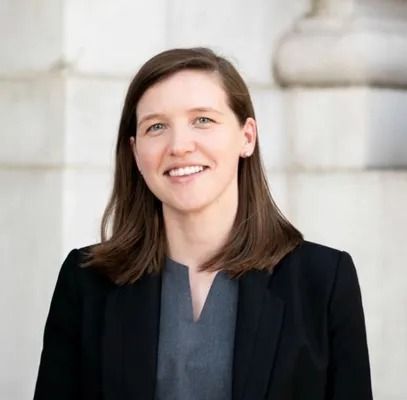 Smiling woman in a black blazer standing against a light stone wall