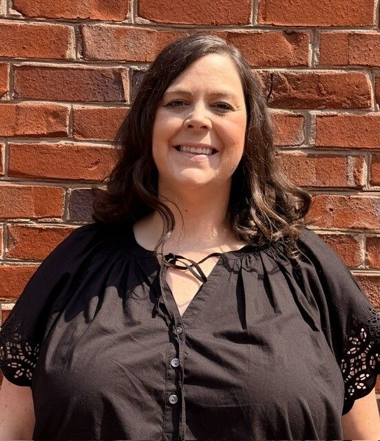Smiling person in a black blouse standing in front of a red brick wall