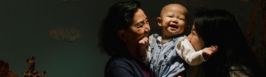 Woman holding a laughing baby beside a mural with animals and people silhouettes