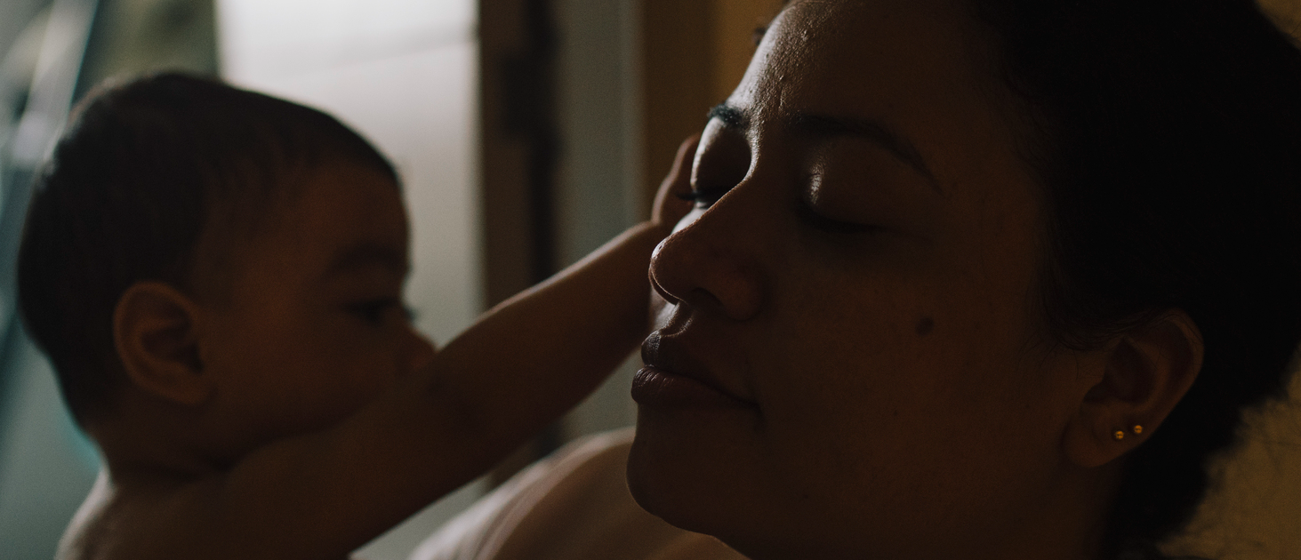 A child reaches toward a woman’s face in a dim, intimate close-up.