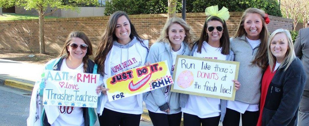 Six smiling women hold handwritten signs outdoors, including a sign reading “Remember Tracie.”