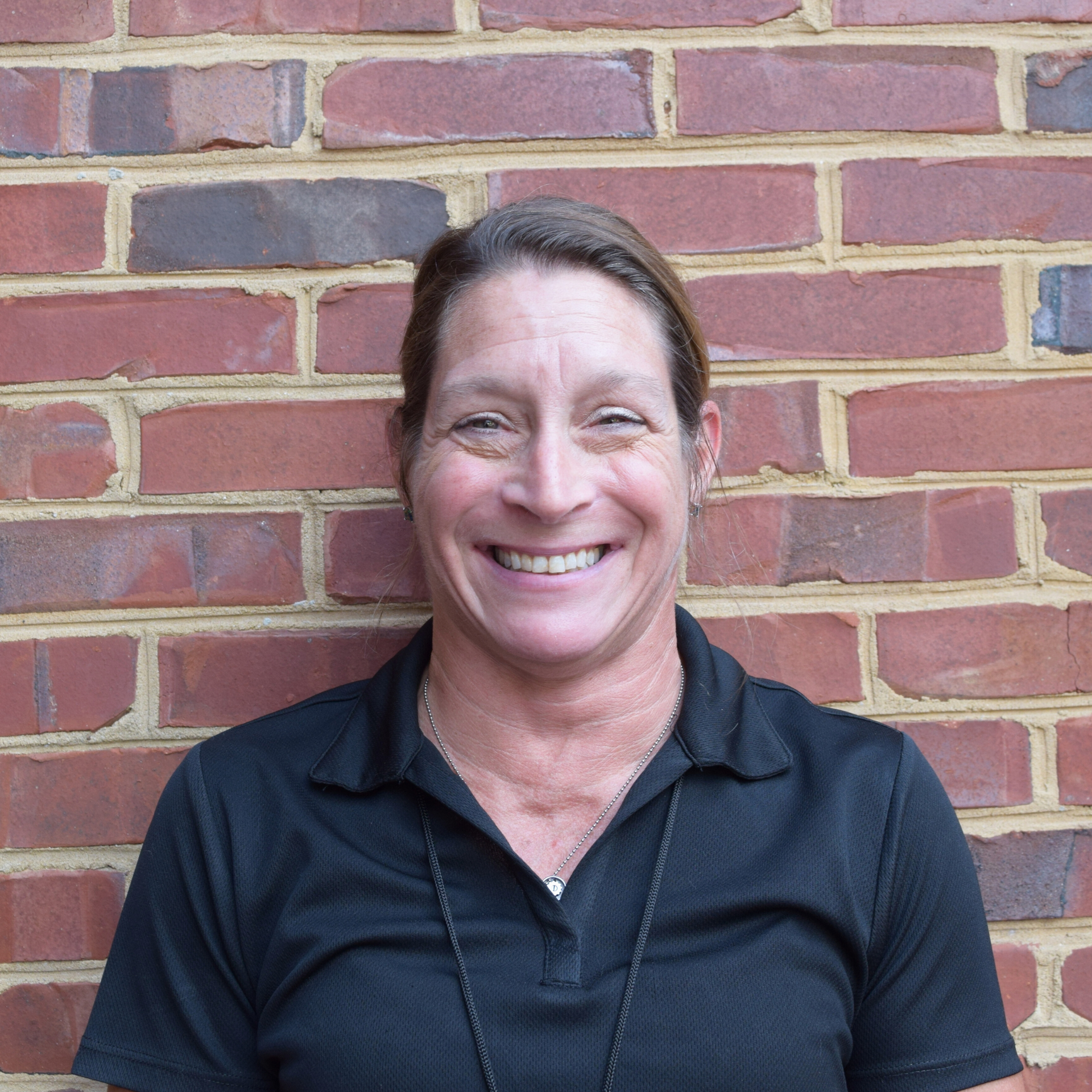 Smiling person in a dark shirt standing against a red brick wall