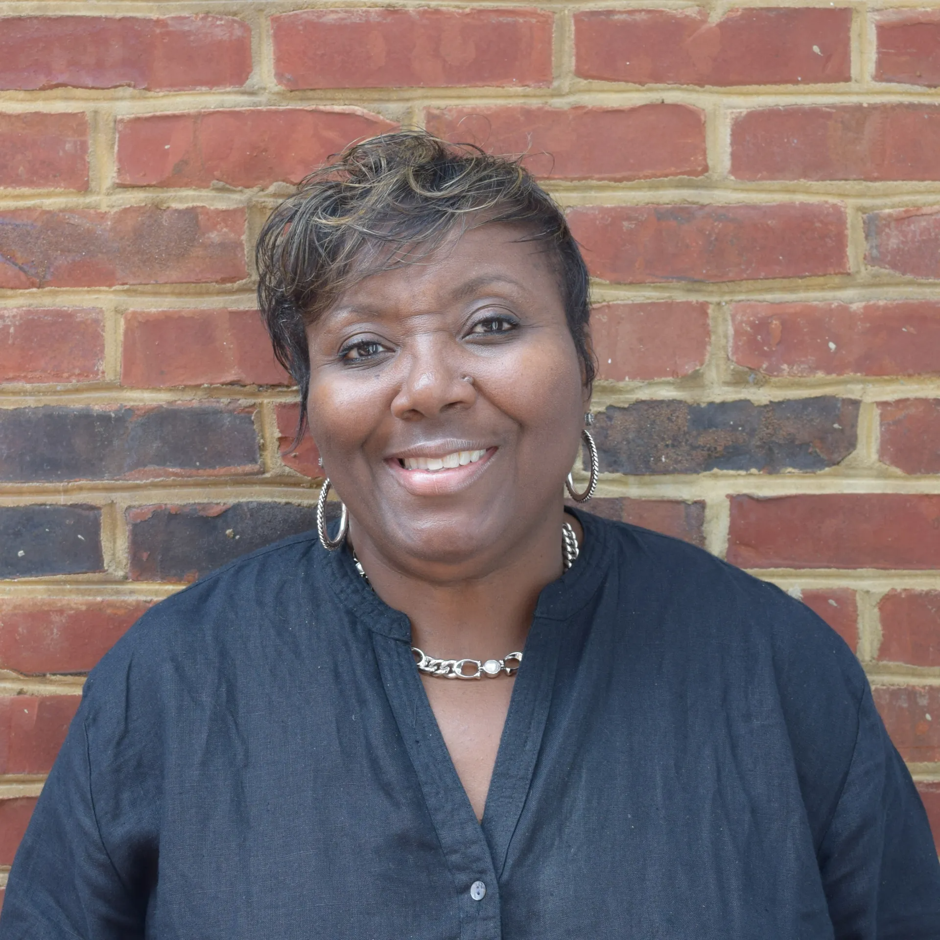 Smiling person in a dark blouse standing before a red brick wall.
