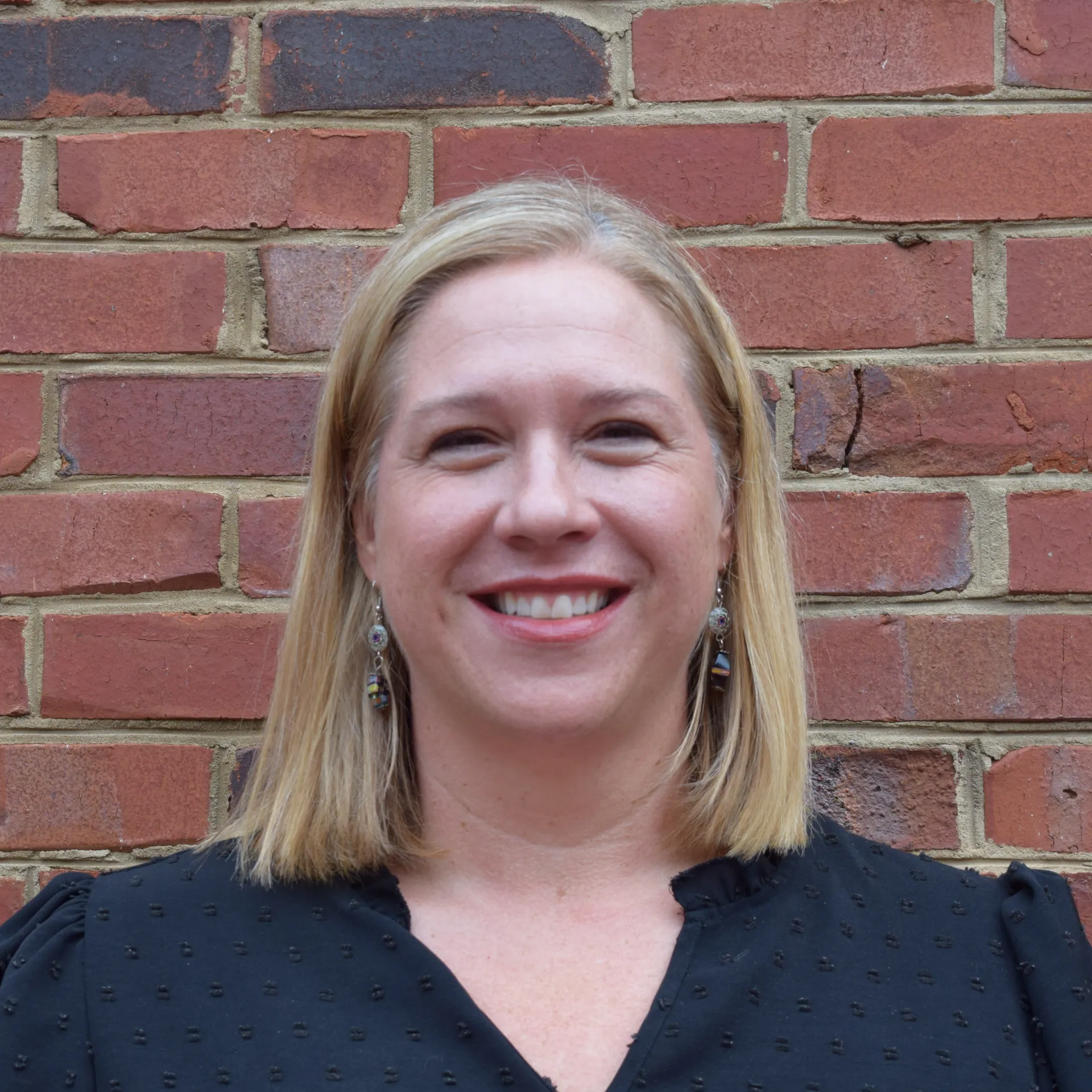 Smiling woman with blonde hair standing against a brick wall