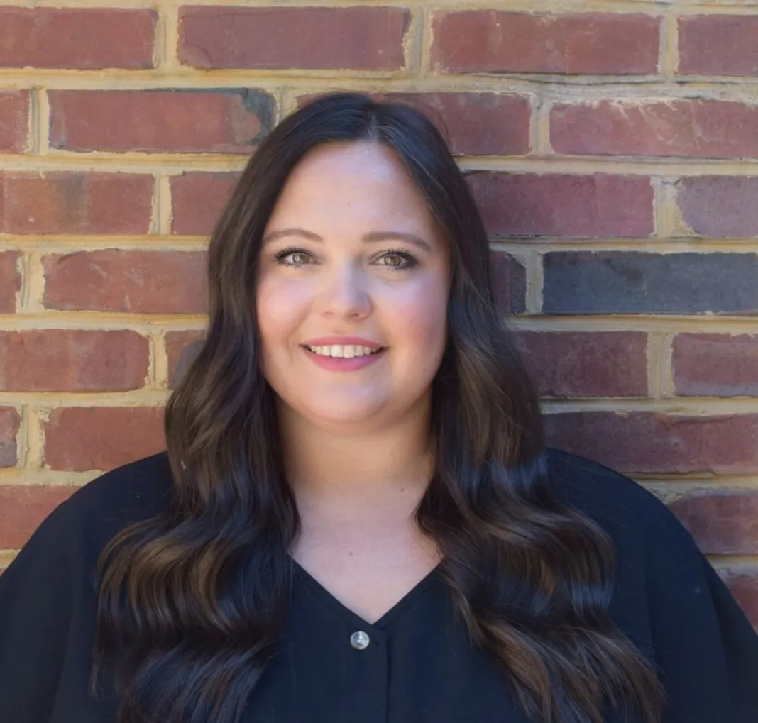 Portrait of a smiling woman with long dark hair standing against a brick wall