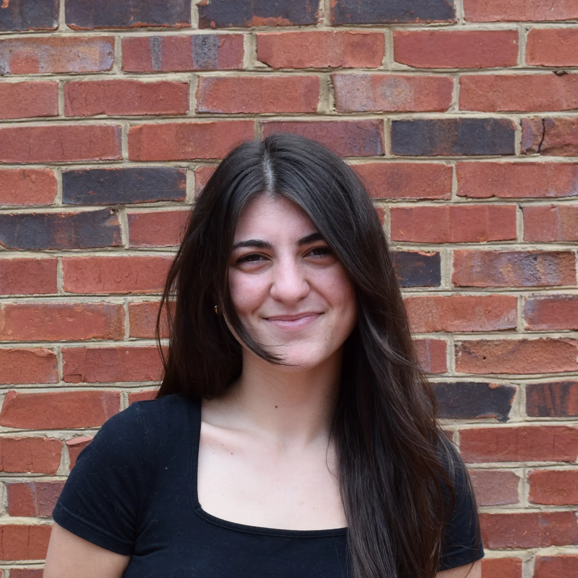 Smiling woman with long dark hair in a black top standing against a brick wall