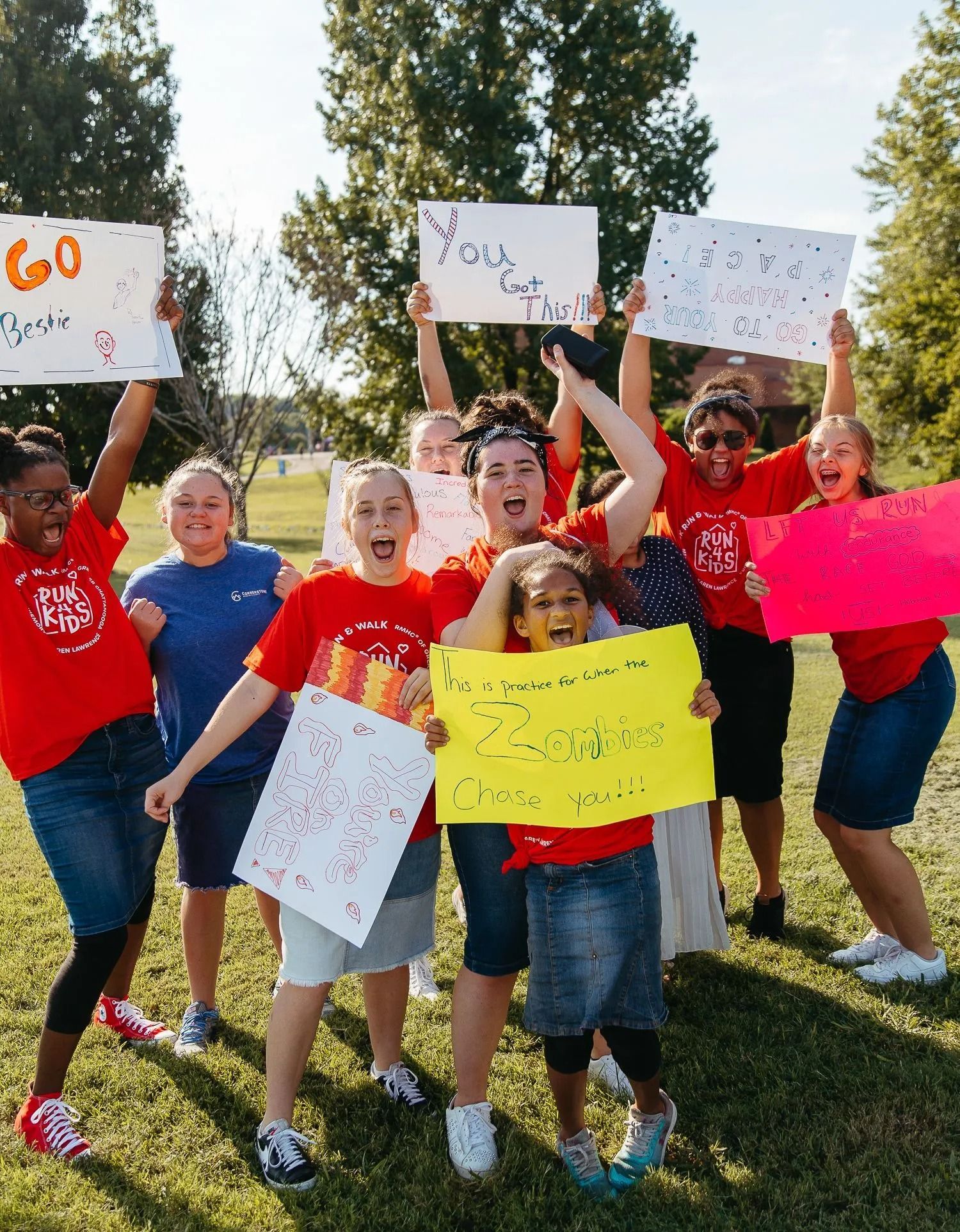Group of people in red shirts holding colorful signs outdoors on a sunny day.