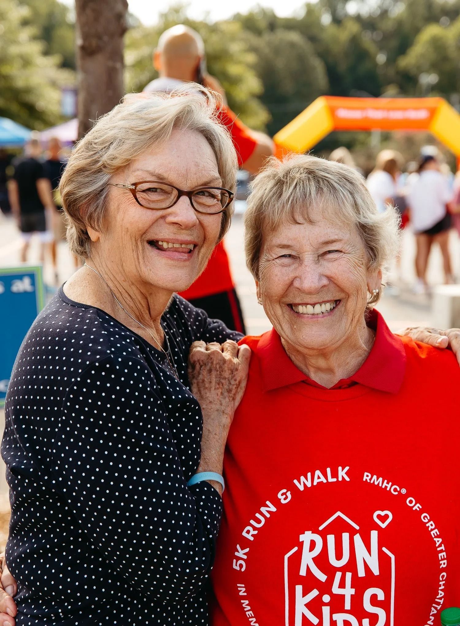 Two smiling people at a Run 4 Kids event, one in a red shirt and one in a navy polka-dot top
