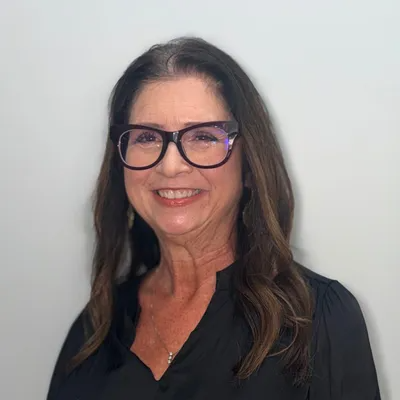 Woman with dark hair and glasses smiling against a plain light background
