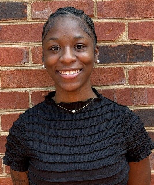 Smiling person in a black textured top standing against a red brick wall