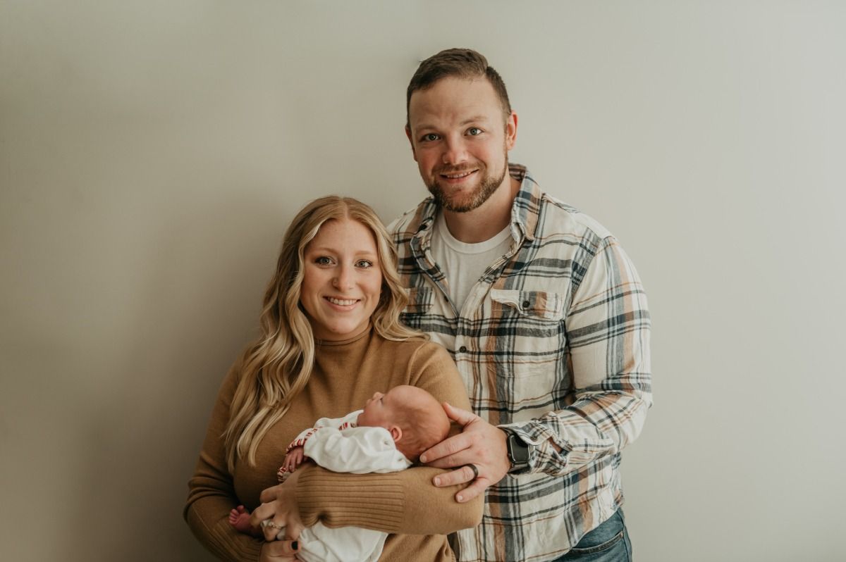 Couple holding a newborn baby against a plain beige wall