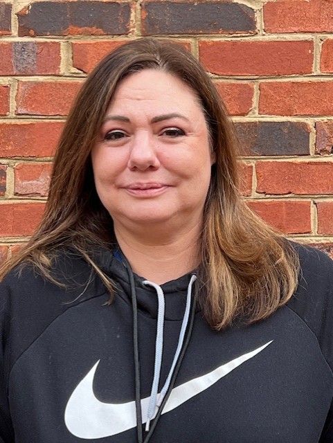 Woman standing against a brick wall, wearing a black Nike hoodie and slight smile.