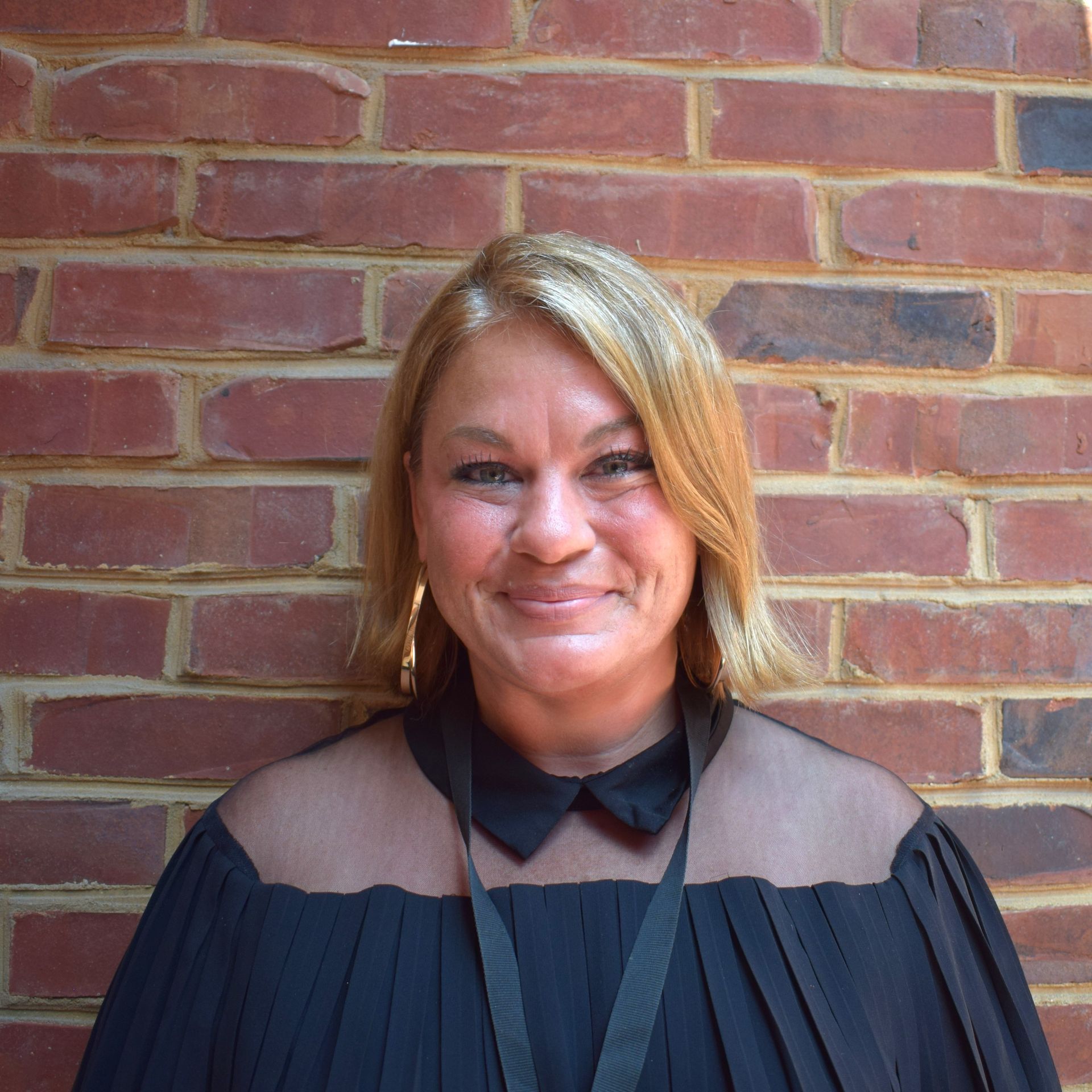 Smiling woman in a black top standing against a red brick wall