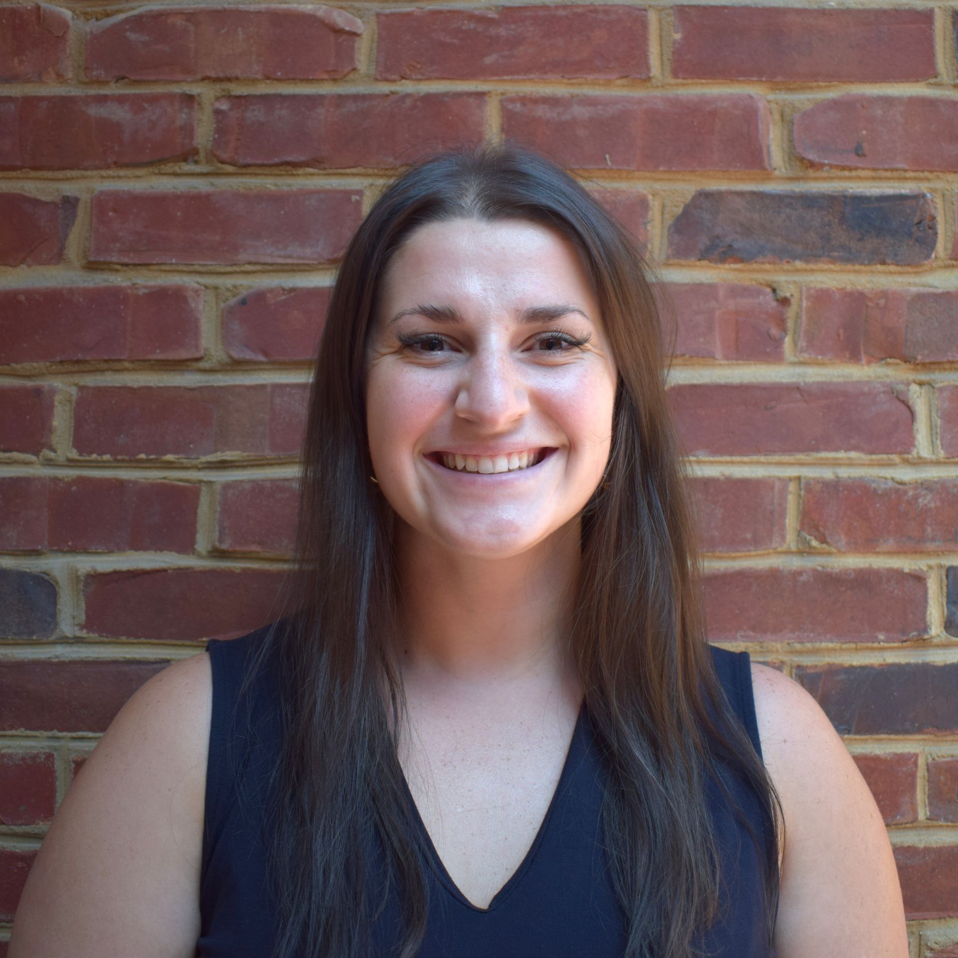 Smiling person in a black shirt standing against a brick wall