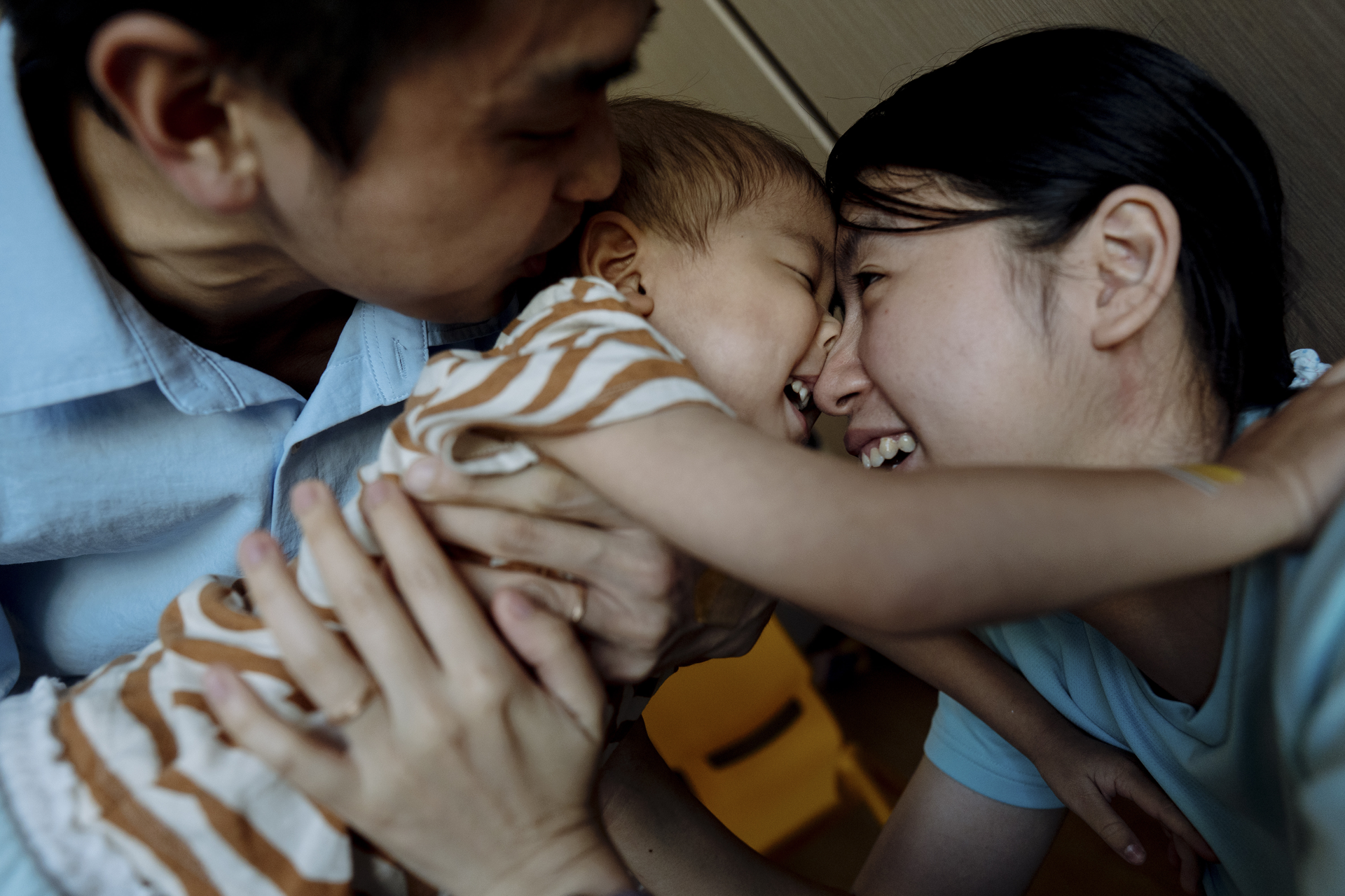 A family cuddles close together, smiling and nuzzling a baby wrapped in a striped blanket.