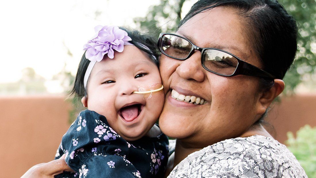 A smiling mom presses her cheek to her laughing young daughter.