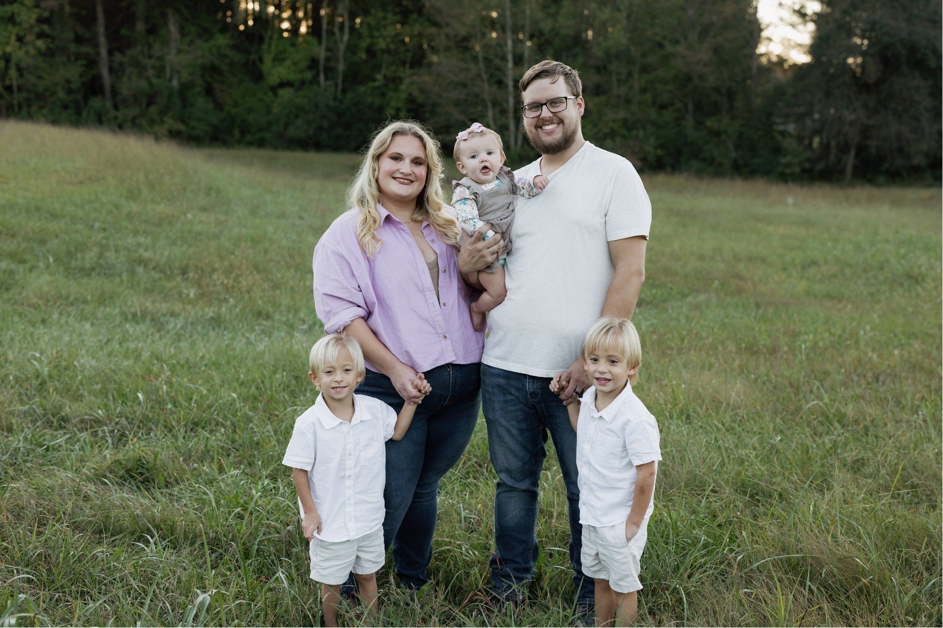 The Hall family, mom and dad holding their baby with their twin boys standing in front, outdoors in a grassy field.