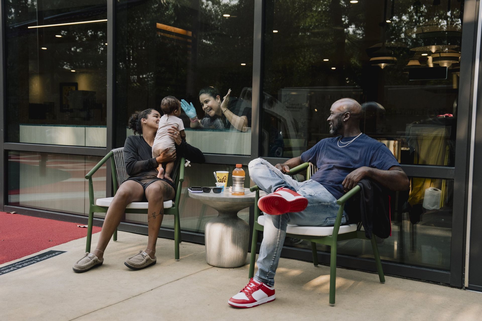 Families relax together on an outdoor patio, a mom holding her toddler while they talk and laugh.