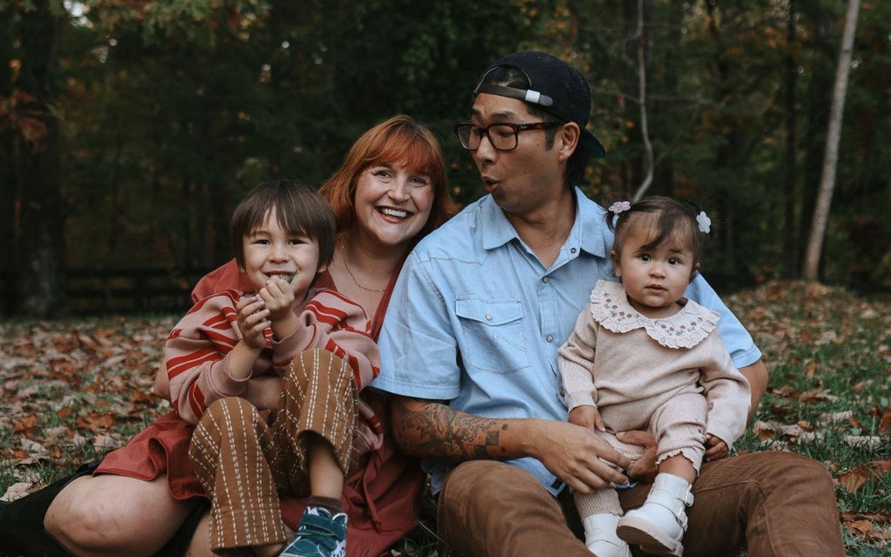 A mom and dad sit in autumn leaves with their young son and baby daughter.