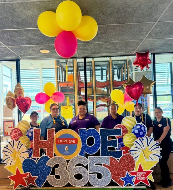 Woman in McDonald’s uniform holding a “Give to have families closer” pamphlet outdoors