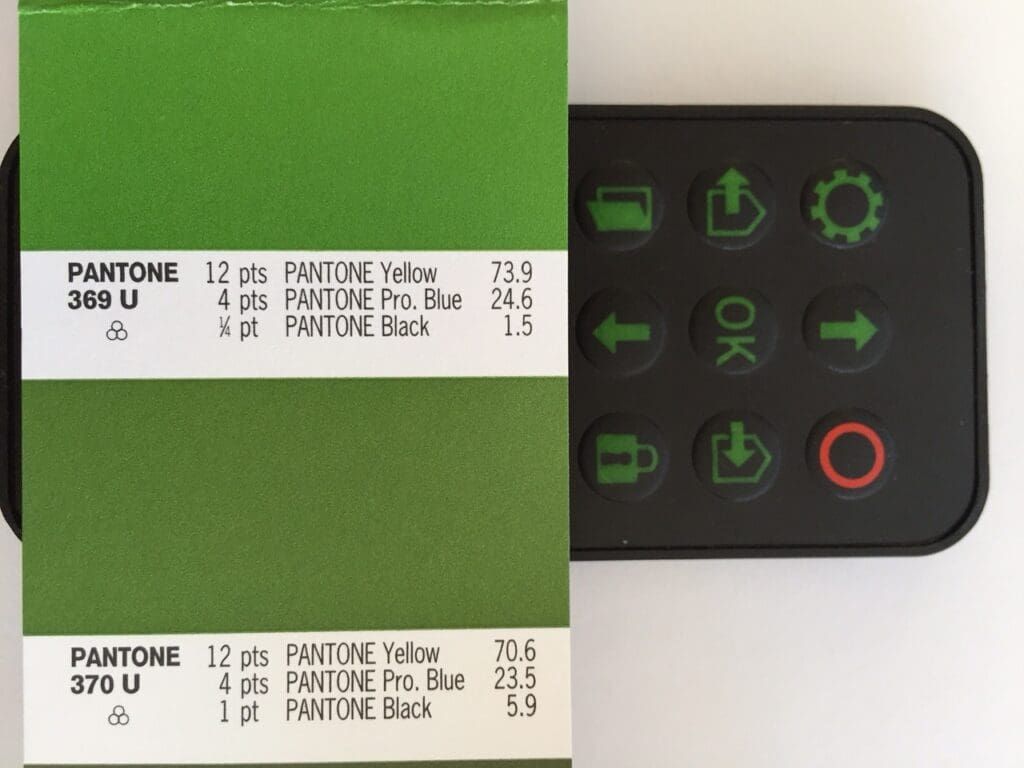 Green color swatch next to a black control panel with buttons, showing color breakdowns for Pantone 389U and 370U.