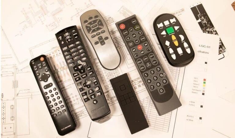 Assortment of various TV remote controls, mostly black, scattered on a white surface.