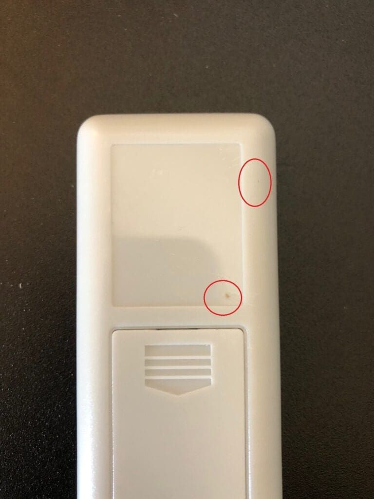 White remote control, with two small red circles indicating imperfections on its surface.