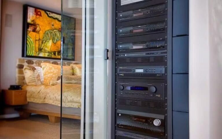 Audio/video equipment rack next to a bedroom, behind a glass door.