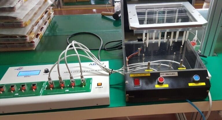 A testing machine with probes connected to a white control unit on a green table.