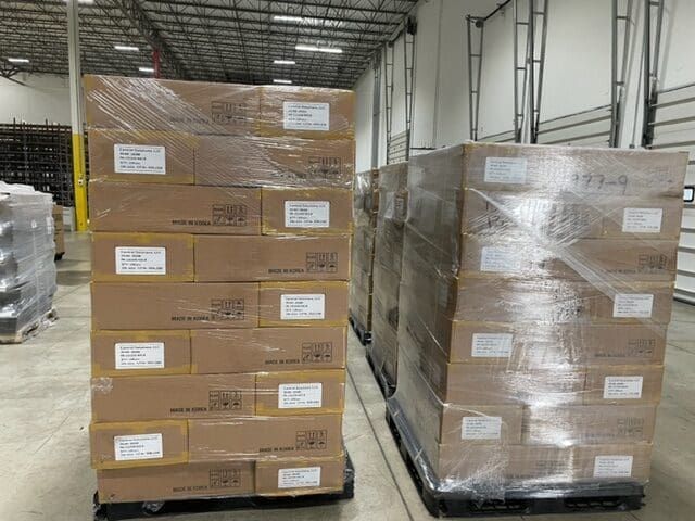 Pallets of boxes wrapped in plastic wrap inside a warehouse.