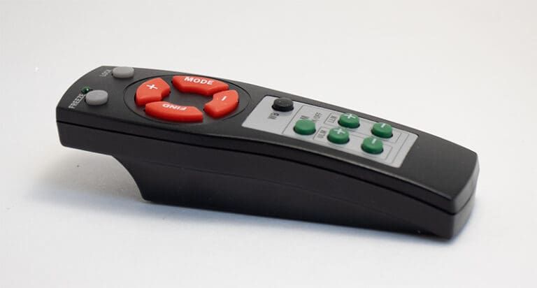 Black remote control with red directional buttons and green function buttons on a white surface.