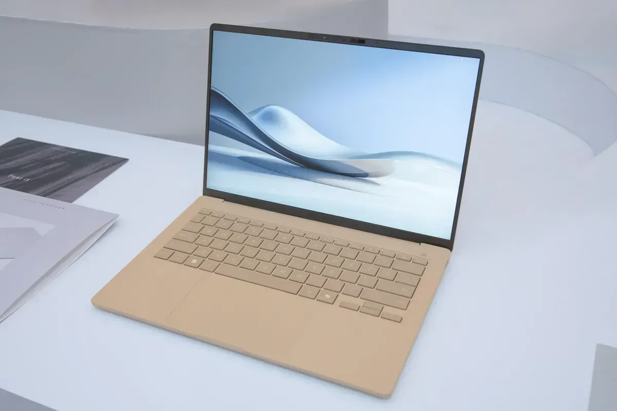 Beige laptop on a white surface, with a wave-themed wallpaper displayed on the screen.
